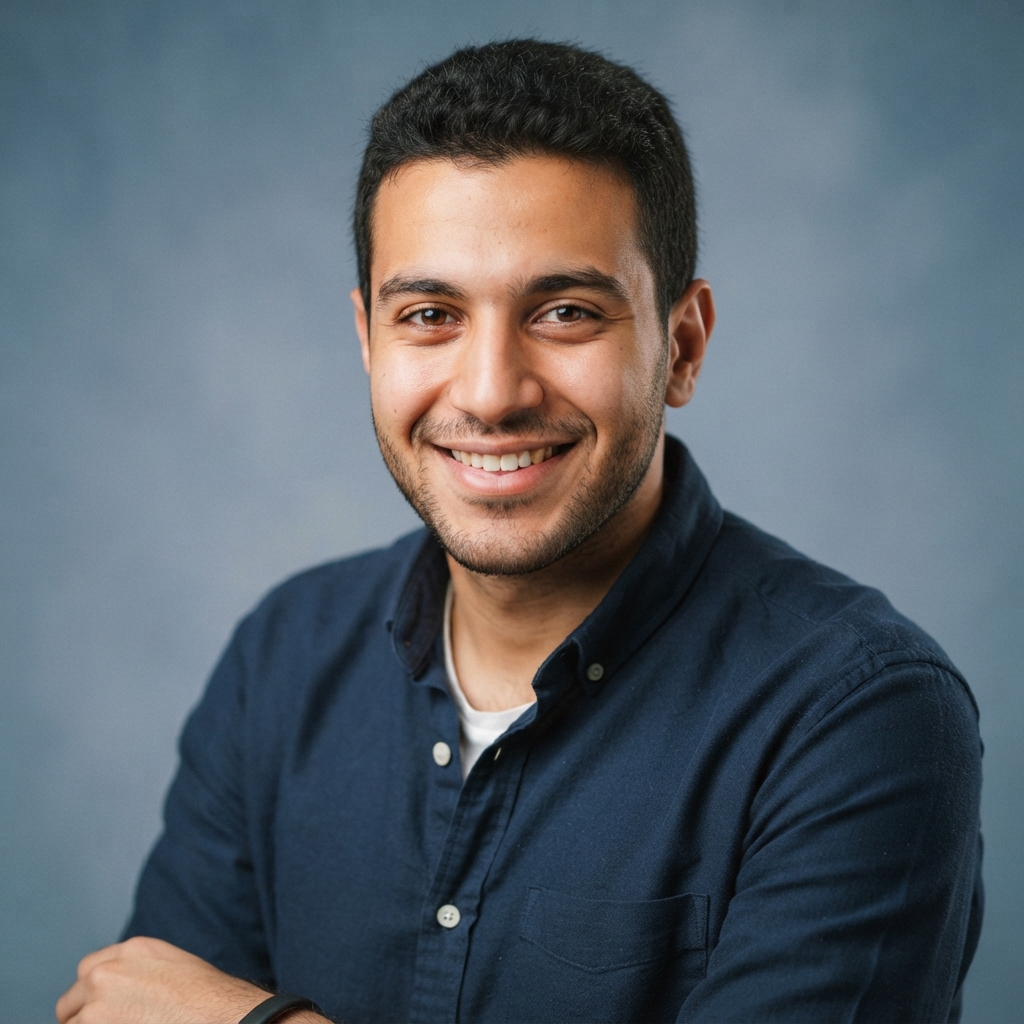 Smiling man in a navy button-up shirt posing against a blue-gray studio background.